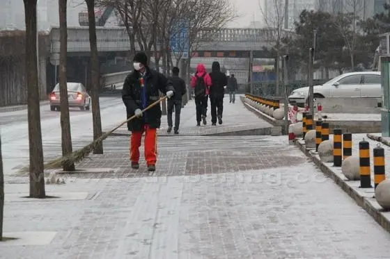 A municipal worker is sweeping the snow from the sidewalk.