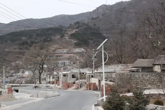 Parallelled by a gully, a wide main road passes through the village with solar-powered street lights. Farmhouses perched on the hillsides orderly