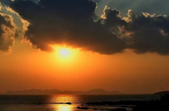 The rising Sun is up under clouds.