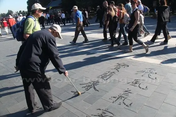 An old man writing Chinese calligraphy with a big brush dipped in water