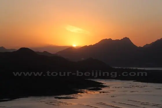 the rising sun half over the mountain line in the distance